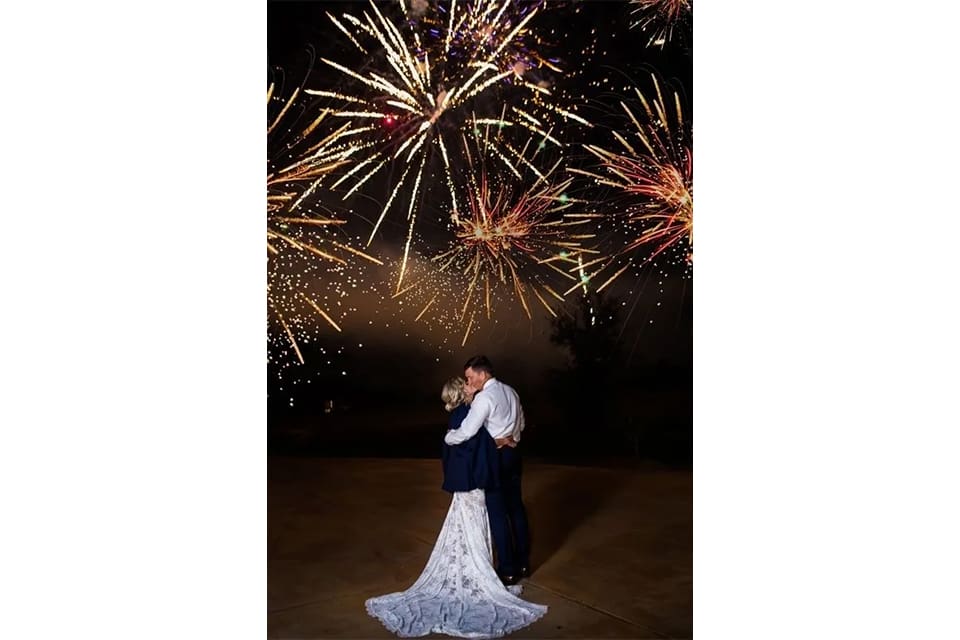 A bride and groom kissing in front of fireworks