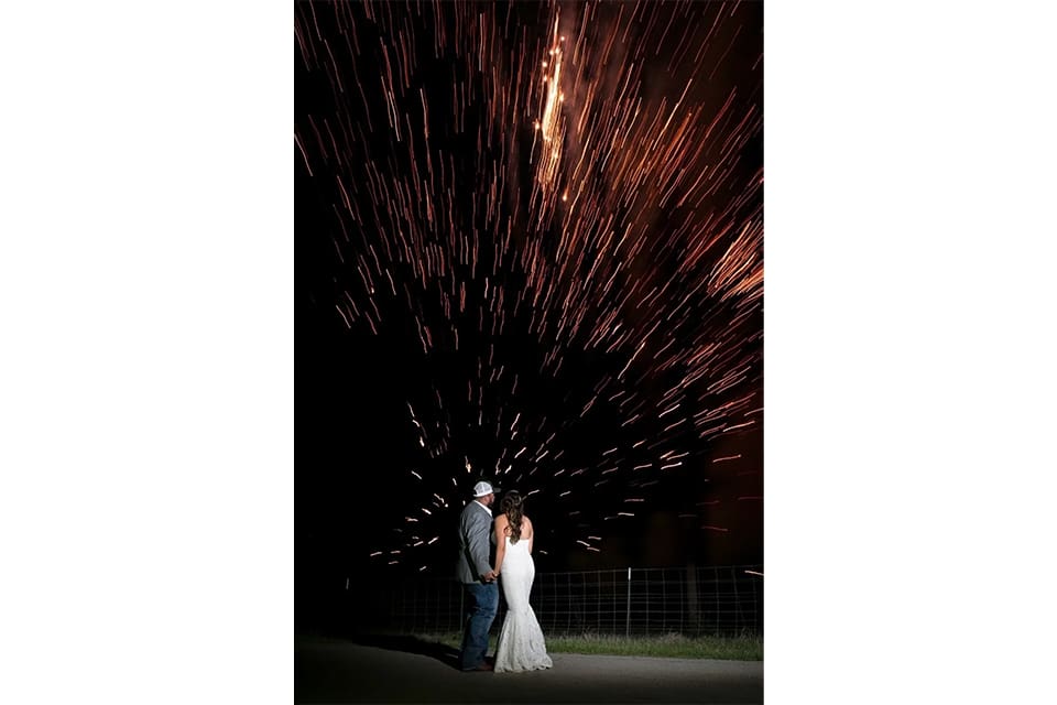 A bride and groom standing in front of fireworks