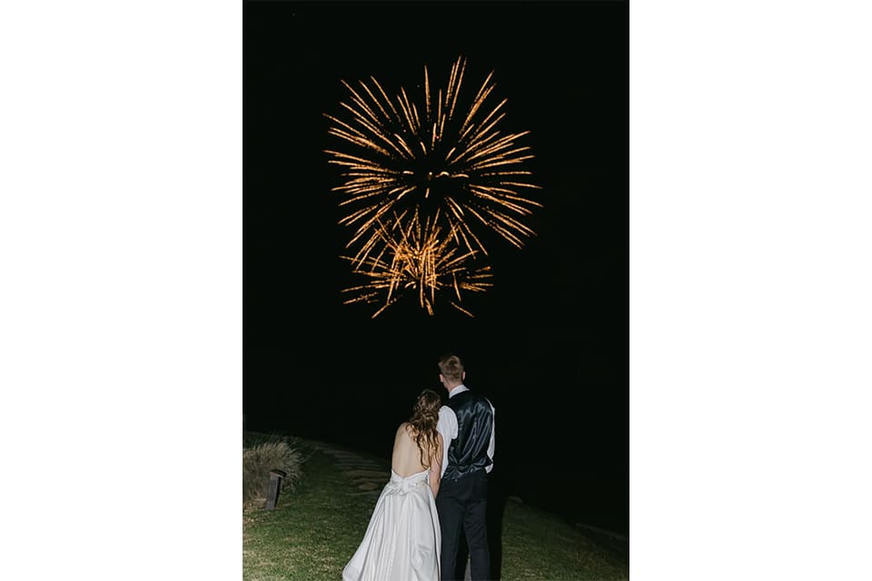 A bride and groom standing in front of fireworks